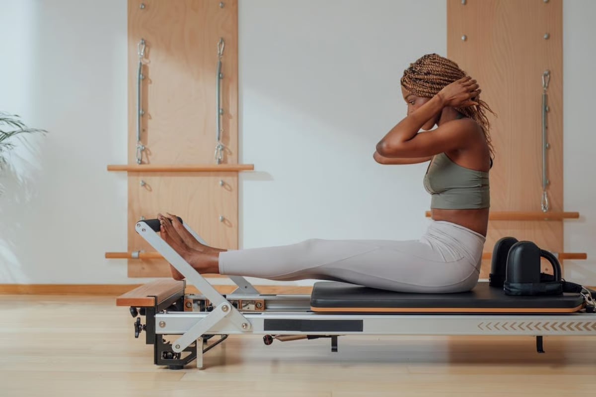 Woman performing a Pilates exercise on a reformer machine in a bright studio with wooden wall fixtures